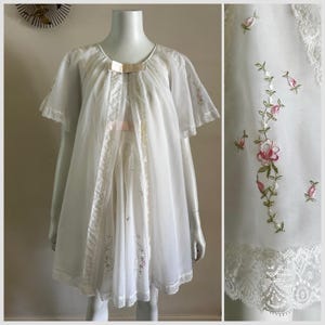 May include: A white sheer robe featuring short flutter sleeves, a round neckline with a pale pink ribbon bow, and vertical lace trim panels. The garment is adorned with delicate pink and green floral embroidery and finished with a scalloped lace hem.