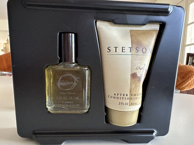 May include: A black gift box set containing a clear glass bottle of aftershave with a brown cap and a white tube of aftershave conditioner. The aftershave bottle has the text "After Shave 5 FL OZ 14.7 ml" and the conditioner tube has the text "STETSON AFTER SHAVE CONDITIONING 2 FL OZ 60 ml".