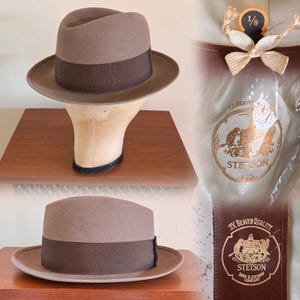 May include: A brown fedora hat with a dark brown band, displayed on a hat form. The hat has a classic design with a slightly curved brim. The Stetson label is visible on the packaging, indicating a high-quality product. The hat is likely made of felt.