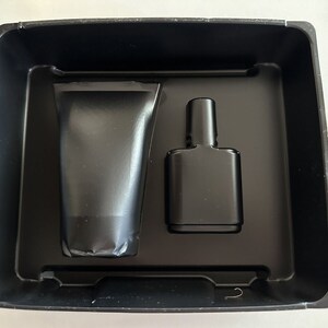 May include: A black plastic tray with two black containers. One container is a tube and the other is a bottle.