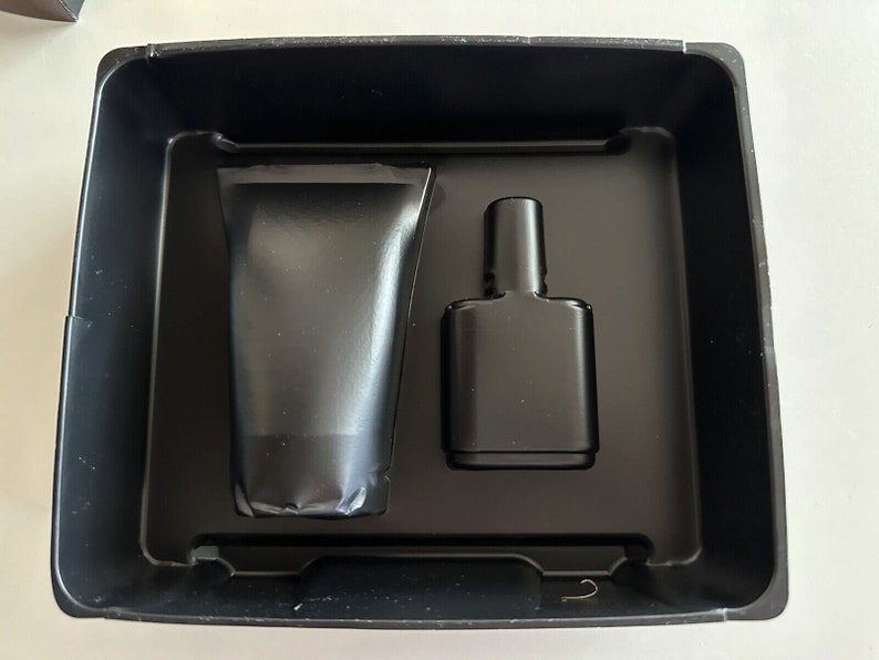 May include: A black plastic tray with two black containers. One container is a tube and the other is a bottle.