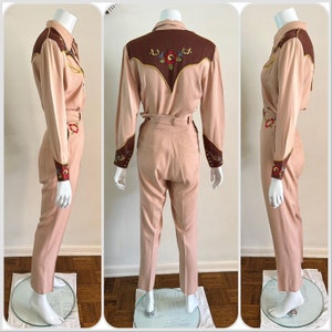 Pu&ograve; includere: Un completo in due pezzi di colore rosa chiaro con ricami marroni sul collo e sui polsini. La camicia ha un colletto a punta e maniche lunghe. I pantaloni hanno vita alta e gamba dritta.