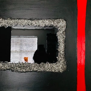 May include: A black and silver framed mirror with a view of a window with white blinds and a black silhouette of a building in the background. The mirror is set against a black background with a red vertical stripe on the right side.