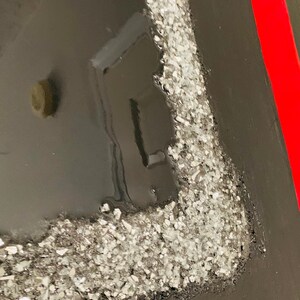 May include: Close-up of a black canvas with a red stripe on the right side. The canvas has a silver glitter border on the left side.