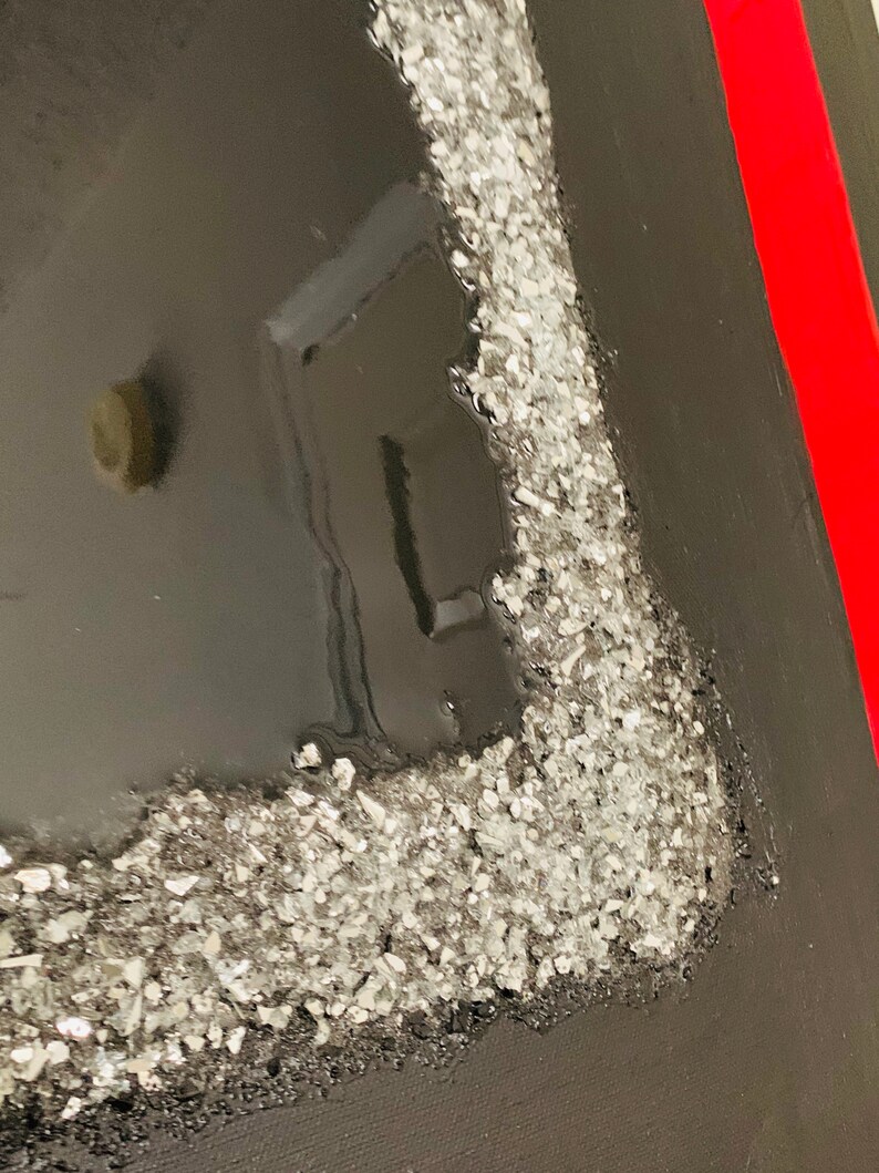 May include: Close-up of a black canvas with a red stripe on the right side. The canvas has a silver glitter border on the left side.