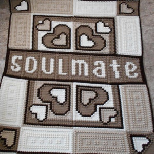 May include: A crocheted blanket in brown, beige and white featuring a heart design and the word "soulmate" in white lettering.