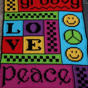 May include: A colourful crocheted wall hanging with the words "groovy", "love", "peace" and smiley faces. The hanging is made with different coloured squares and chequered patterns.