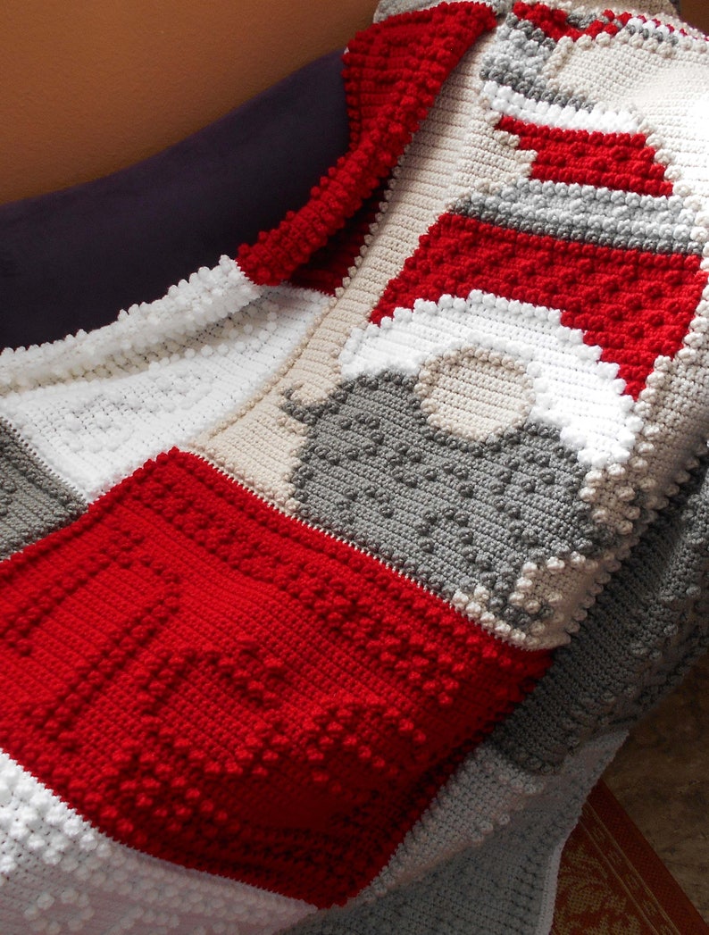 May include: A crocheted blanket with a red, white, and gray color scheme. The blanket is made with a textured stitch that creates a bumpy surface.