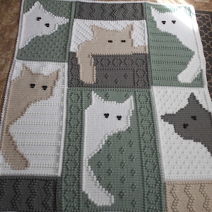Puede incluir: Una manta de ganchillo con un diseño de patchwork de gatos en varias poses. Los gatos están hechos a ganchillo en blanco, beige y gris sobre un fondo verde.