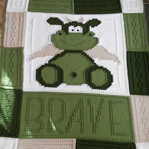 May include: A green crocheted baby blanket with a green and white crocheted animal in the center. The animal has a large head with big eyes and a small body. The blanket is made of squares with different patterns. The word "LOVE" is crocheted in green on the bottom of the blanket.