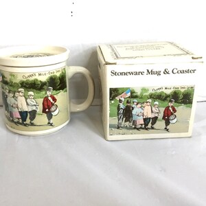 Könnte beinhalten: Ein Steinzeug-Tassen- und Untersetzer-Set mit einer Vintage-Illustration von marschierenden Kindern. Die Tasse hat einen Henkel und einen Deckel. Auf der Box steht "Stoneware Mug & Coaster" und "Clarks Mile-End Shoe Co."