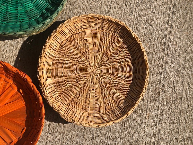 May include: A round, woven wicker basket with a natural brown color. The basket is made of thin, tightly woven strips of wicker, creating a smooth, even surface.
