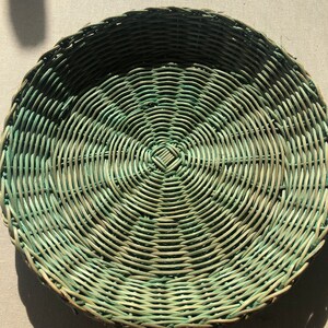 May include: A round woven wicker basket with a green and natural color pattern. The basket is made of natural materials and has a circular shape.