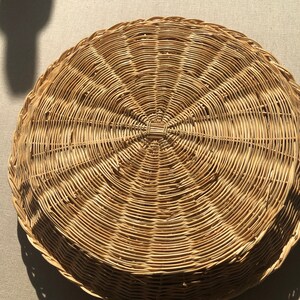May include: A round, woven wicker tray with a natural brown color. The tray has a circular design with a raised center.