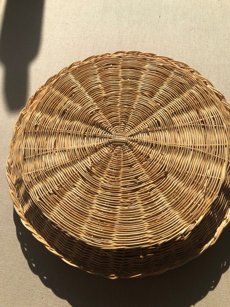 May include: A round, woven wicker tray with a natural brown color. The tray has a circular design with a raised center.