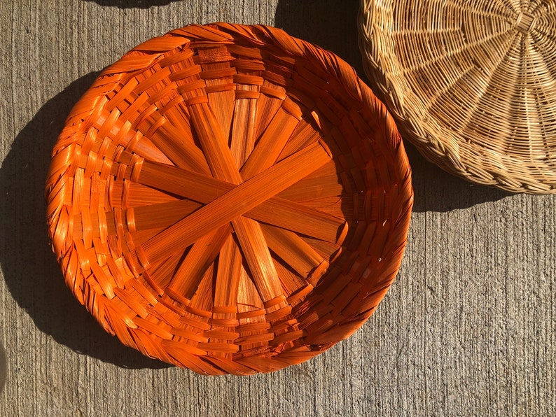 May include: A round, woven basket with a bright orange color. The basket is made of natural materials and has a unique, intricate design.