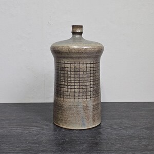 Könnte beinhalten: Eine Keramikvase mit grauer und brauner Glasur. Die Vase hat ein Gittermusterdesign und eine abgerundete Form.