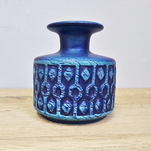 Pode incluir: Um vaso de cerâmica azul com um padrão geométrico texturizado. O vaso tem uma base larga, um corpo cilíndrico e um pescoço alargado. A cor transita de um turquesa mais claro para um azul mais escuro.