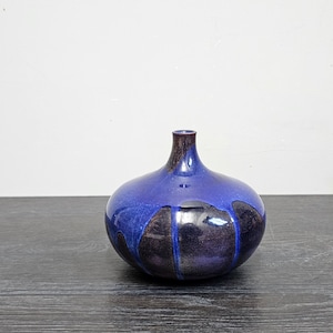 Puede incluir: Un pequeño jarrón de cerámica azul y negro con cuerpo redondeado y cuello estrecho. El jarrón tiene un acabado brillante y un diseño abstracto único.