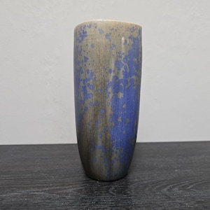 May include: A tall, cylindrical ceramic vase with a mottled glaze in shades of blue and brown. The vase has a speckled, textured surface.