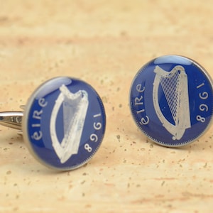 Op de afbeelding: Een paar manchetknopen met een blauwe geëmailleerde Ierse munt met een zilveren harp en de tekst "EIRE 1961".
