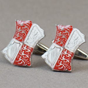 May include: A pair of silver cufflinks with red and white enamel. The cufflinks feature a shield with a harp and lions.