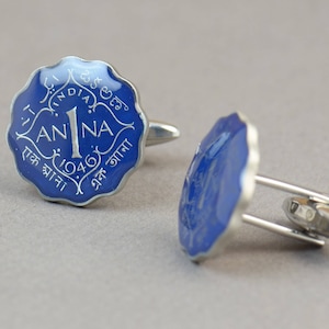 May include: A pair of silver cufflinks with a blue enamel face. Each cufflink features a scalloped edge and the text "1 ANNA 1946" in white. The cufflinks have a classic, elegant design.