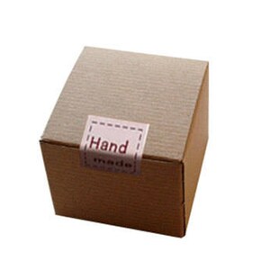 May include: A brown cardboard box with a white label that says "Hand Made".