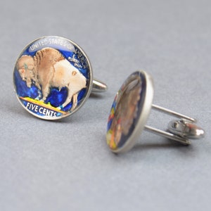 May include: A pair of silver cufflinks featuring a vintage American five-cent coin with a buffalo design. The coin is encased in resin and has a blue and yellow background.