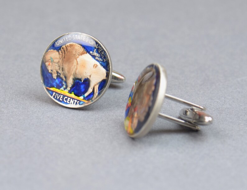May include: A pair of silver cufflinks featuring a vintage American five-cent coin with a buffalo design. The coin is encased in resin and has a blue and yellow background.