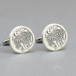 May include: A pair of silver cufflinks with a detailed design of a bison standing in a forest with stars and a crescent moon in the background.