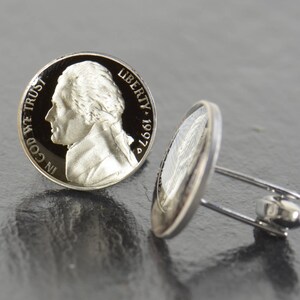 May include: A pair of silver cufflinks featuring a vintage 1997 US nickel coin with the profile of Thomas Jefferson and the inscription "IN GOD WE TRUST" on one side and "LIBERTY 1997" on the other side.