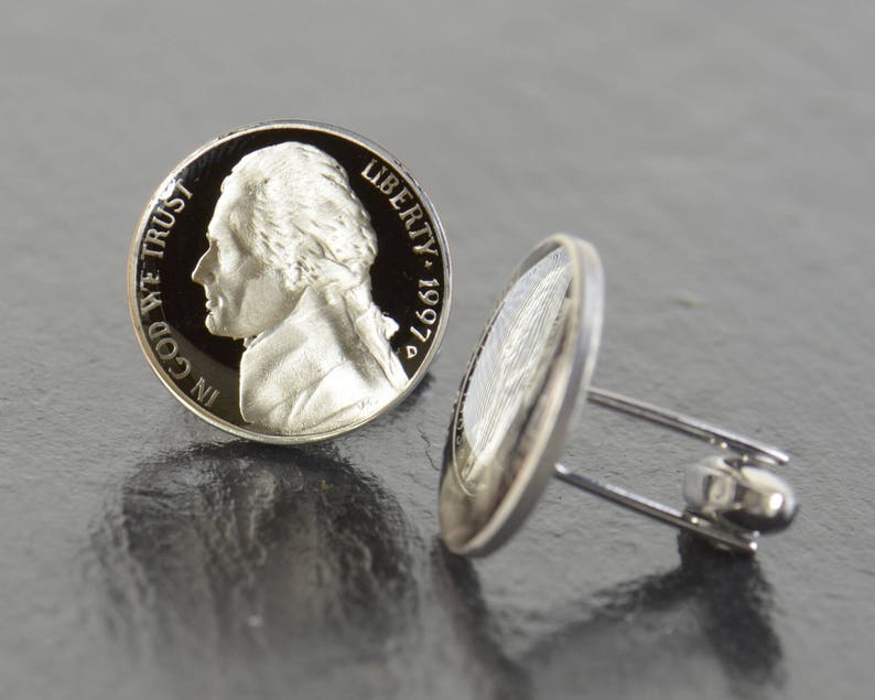 May include: A pair of silver cufflinks featuring a vintage 1997 US nickel coin with the profile of Thomas Jefferson and the inscription "IN GOD WE TRUST" on one side and "LIBERTY 1997" on the other side.