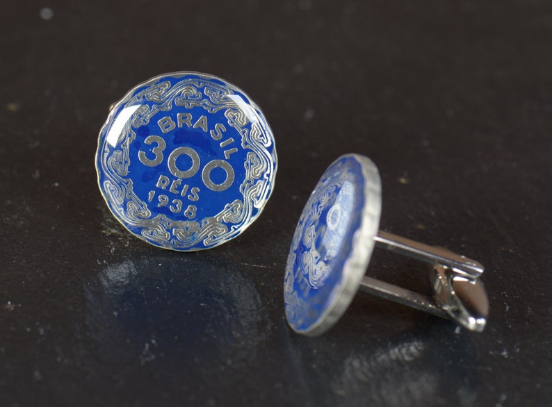 May include: A pair of cufflinks featuring a blue enamel coin with the text "BRASIL 300 REIS 1938" in silver lettering.