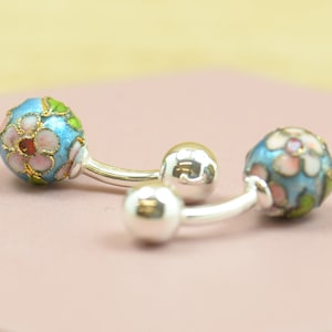 May include: A pair of silver cufflinks with blue enamel and floral designs. The cufflinks have a round shape and are decorated with pink and green flowers.