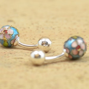 May include: A pair of silver cufflinks with blue enamel and pink and white floral designs.