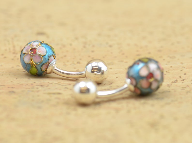 May include: A pair of silver cufflinks with blue enamel and pink and white floral designs.