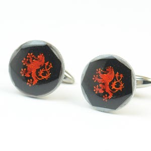 May include: A pair of silver cufflinks with a black background and a red lion crest design.