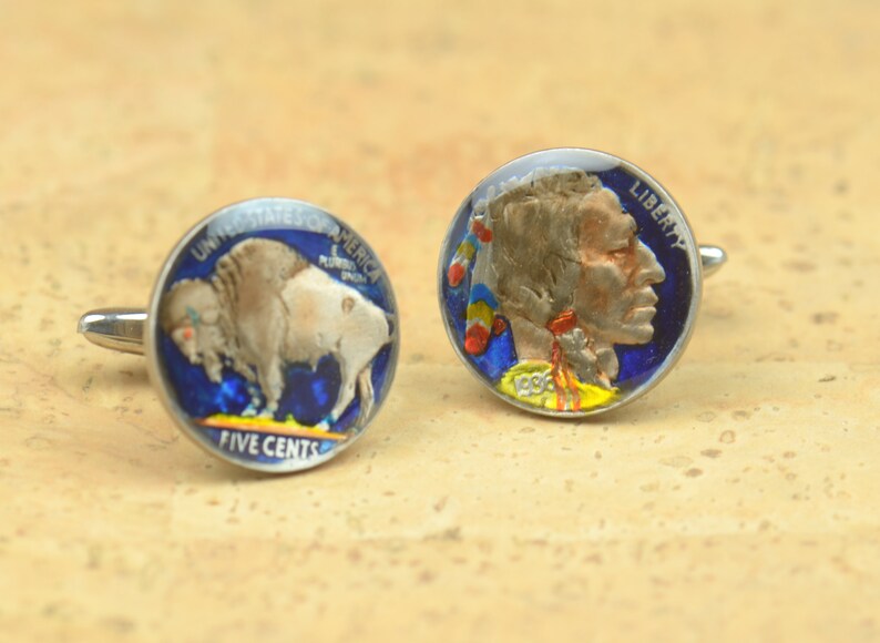 May include: A pair of cufflinks featuring a vintage American Indian Head nickel and a vintage Buffalo nickel. The coins are painted with blue, red, yellow, and white accents.