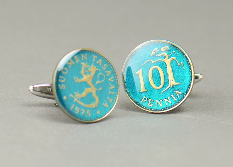 Pode incluir: Um par de bot&otilde;es de punho com moedas finlandesas antigas. As moedas s&atilde;o azuis com detalhes dourados e apresentam o texto "SUOMEN TASAVALTA 1975" e "10 PENNI&Auml;".