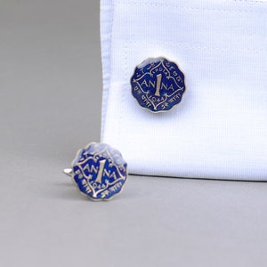 May include: A pair of vintage cufflinks with a blue and gold coin design. The cufflinks are shaped like a coin with the word "ANNA" and the number "1" in the center. The year "1944" is also visible.