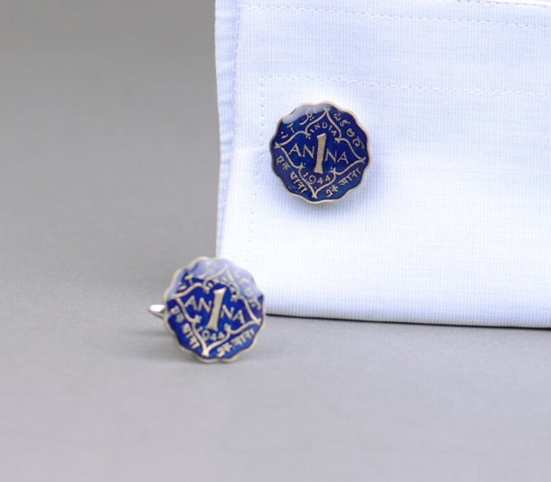 May include: A pair of vintage cufflinks with a blue and gold coin design. The cufflinks are shaped like a coin with the word "ANNA" and the number "1" in the center. The year "1944" is also visible.