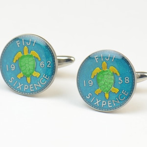 May include: A pair of cufflinks featuring a turquoise blue coin with a green and yellow turtle design. The coin reads "FIJI 1962 SIXPENCE".