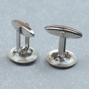 May include: A pair of silver cufflinks with a round, white, and blue design. The cufflinks have a silver oval-shaped bar with a small square in the center.