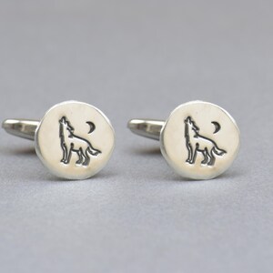 May include: A pair of silver cufflinks with a wolf howling at the moon design.