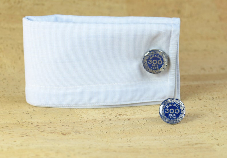 May include: A pair of silver cufflinks with a blue enamel design. The cufflinks feature the text "BRASIL 300 DEIS 1938".