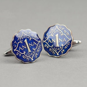 May include: A pair of cufflinks featuring a blue and silver design. The cufflinks are shaped like vintage Indian coins, with the text "1 ANNA" and the year "1944" visible. The background is a solid gray.