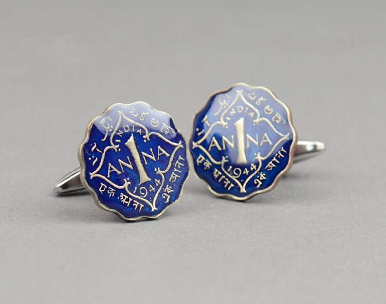 May include: A pair of cufflinks featuring a blue and silver design. The cufflinks are shaped like vintage Indian coins, with the text "1 ANNA" and the year "1944" visible. The background is a solid gray.