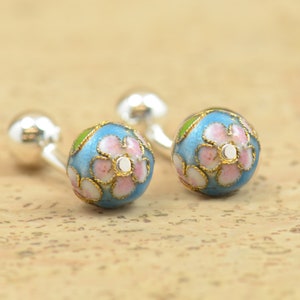 May include: A pair of silver cufflinks with blue enamel and pink flower designs.