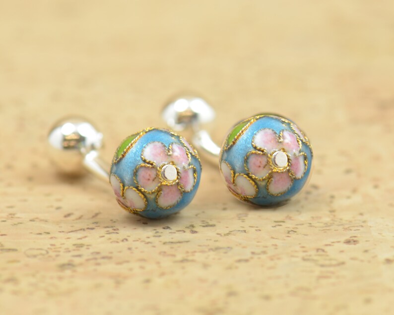 May include: A pair of silver cufflinks with blue enamel and pink flower designs.